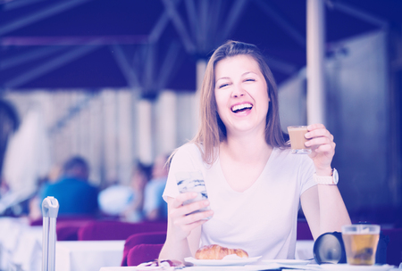 Smiling woman is drinking coffee and chatting in the phone.の写真素材