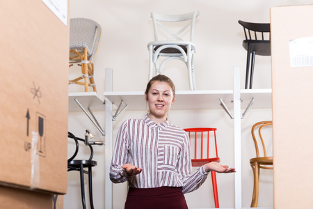 Portrait of young attractive saleswoman welcoming visitors to chair storeの写真素材