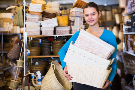 Attractive female standing with wicker basket in decoration and furniture storeの写真素材