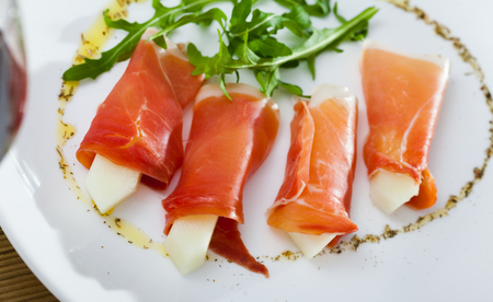 Spanish tasty dish rolls of prosciutto di parma with melon served with arugula at plate, close upの写真素材