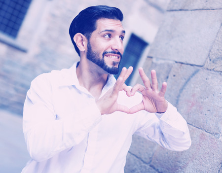 Happy smiling young man showing sign of heart with his fingersの写真素材