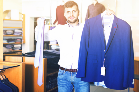 Positive  handsome adult guy  choosing modern jacket in men storeの写真素材