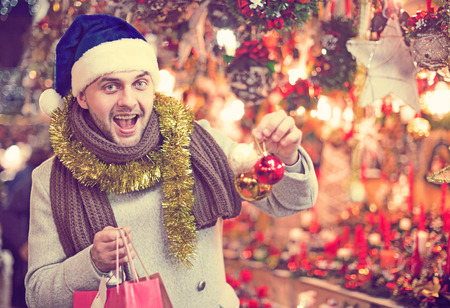 Happy young man in x-mas hat with purchases delighted at Christmas marketの写真素材