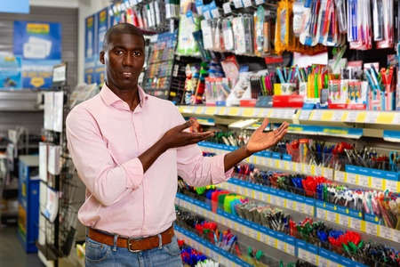 Portrait of young glad cheerful  smiling man customer looking new pen in stationery storeの写真素材