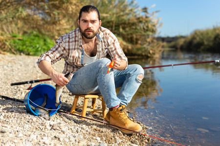 Bearded adult man posing with fish near river in summertimeの写真素材