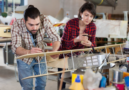 Portrait of happy female and male hobbyists with plane models created by them in aircraft workshop