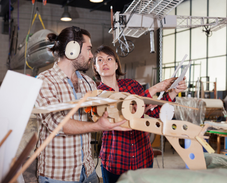 Team of aircraft enthusiasts working in workshop on creating of airplane models, checking design in drawingsの写真素材