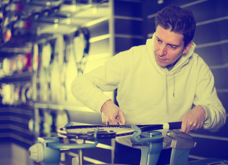 Positive man is correcting tennis rackets in the sportive storeの写真素材