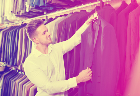 Cheerful positive man choosing new suit in menâs cloths storeの写真素材