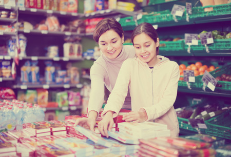 happy woman with daughter choosing delicious cookies in supermarketの写真素材