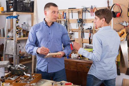 Father and son working with wood tools at workplace in garage
