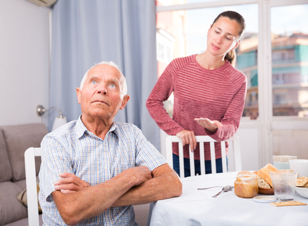 Portrait of unhappy man sitting and having quarrel with daughter at home interiorの写真素材