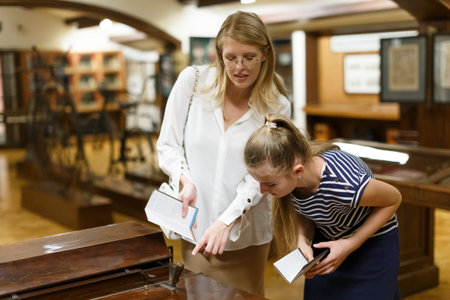 Young woman visitor with daughter with guide book pointing exhibition in museum of art