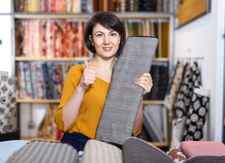 Portrait of happy attractive woman giving thumbs up in fabric shopの写真素材