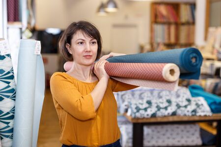 Experienced saleswoman arranging fabric bolts in textile shop, preparing for saleの写真素材