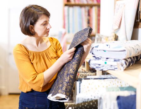 Attractive brunette choosing fabric among diversity on shelves in storeの写真素材