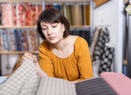 Pensive woman choosing textiles for dressmaking in fabric shop