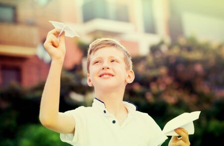 happy boy playing with simple paper airplane toy on sunny day in townの写真素材