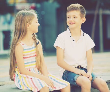 Two smiling kids in preschool age sitting together outdoors in townの写真素材