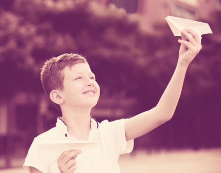 smiling boy in elementary school age playing with flying paper planes outdoorsの写真素材