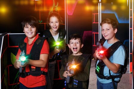 Portrait of happy excited teen kids with laser guns during lasertag game in dark roomの写真素材