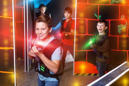 Portrait of  pleasant friendly preteen boy with laser gun having fun on dark lasertag arenaの写真素材