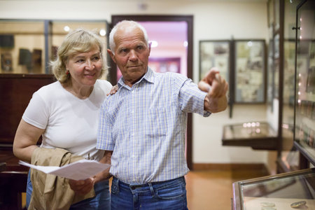 Senior couple holding brochure with information about exhibits on exposition of museum