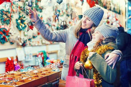 Smiling girl with woman are preparing for Merry Christmas and choosing the gifts for their family outdoor. Focus on both personsの写真素材