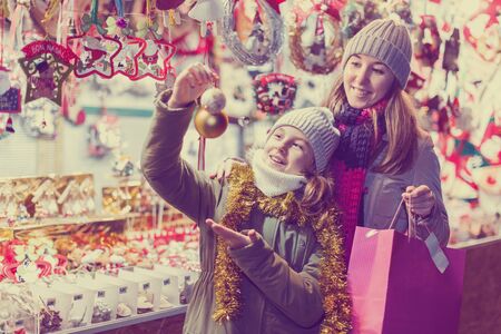 Smiling girl with woman are buying toys for X-mas tree in the market outdoor.の写真素材