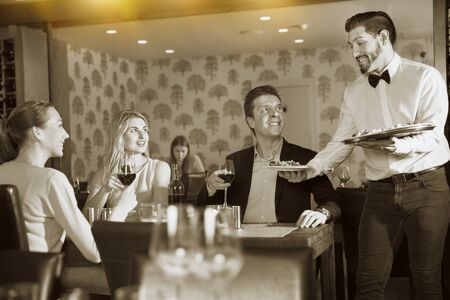 Waiter bringing delicious salads to young visitors of a restaurantの写真素材