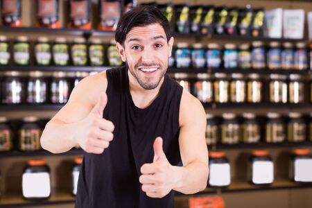 Happy sportman holding thumbs up  in shop of sport nutrition productsの写真素材