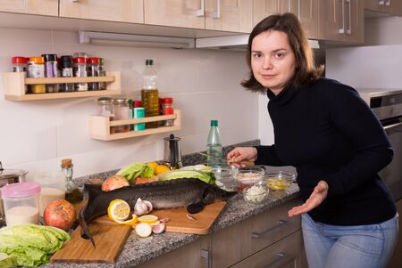 Positive girl  preparing to cook raw sturgeon at home kitchenの写真素材