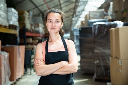 Portrait of female worker in apron with arms crossed standing in warehouseの写真素材