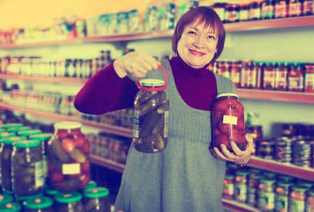 Adult female in food shop holding preserved of cucumbers and tomatoesの写真素材