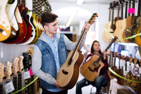 Glad female and male teenagers choosing acoustic guitars in guitar shopの写真素材