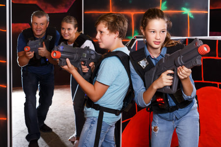 Positive teenage boy and girl with laser guns having fun with adults in dark lasertag roomの写真素材
