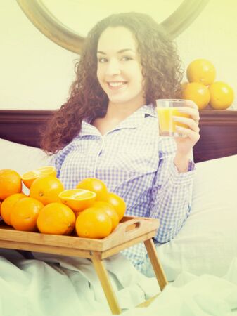 Adult girl posing with orange juice and fruits in bedの写真素材