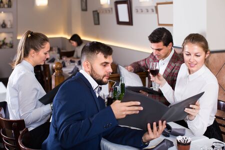 smiling people sitting at table in cozy restaurant, discussing menuの写真素材