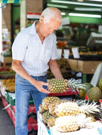 Portrait of smiling older man choosing sweet ripe fruits in farmer marketの写真素材