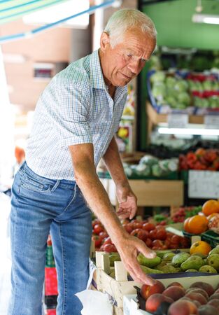 Portrait of smiling older man choosing sweet ripe fruits in farmer marketの写真素材
