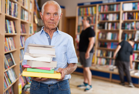 Portrait of elderly male buyer with pile of books in bookshop interior