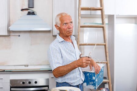 House renovation, elderly man renovating indoor walls with spatula and plasterの写真素材