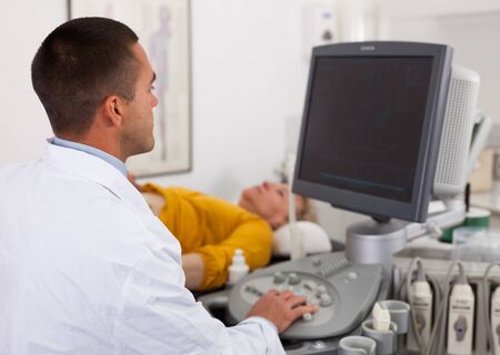 Young man sonographer using ultrasonography machine checking female patient in hospital diagnostic roomの写真素材