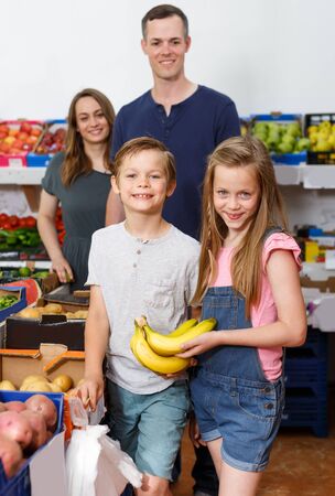 Laughing preteen children holding fresh delicious bananas in supermarketの写真素材