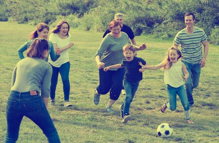 Smiling people of different ages playing football on grassの写真素材