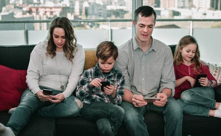 Young smiling cheerful family playing with their smartphones together at homeの写真素材