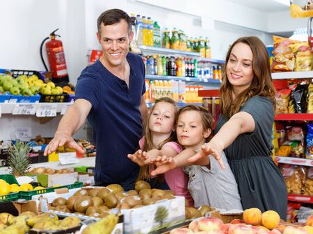 Smiling glad cheerful positive family with kids points to fresh delicious fruits in supermarketの写真素材