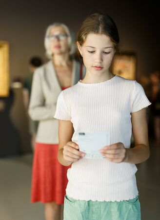 Positive tween girl observing with interest exhibition in art galleryの写真素材