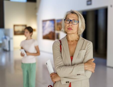 Intelligent senior female looking with interest at exposition in historical museumの写真素材