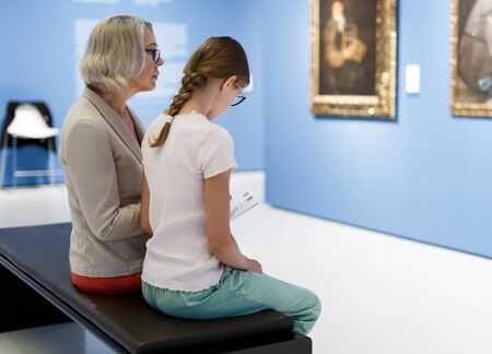 Senior woman and tween girl reading brochure with exhibition program in museum of artの写真素材